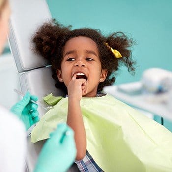 Little girl in dental chair pointing to smile