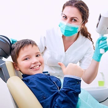 Young boy in dental chair giving thumbs up