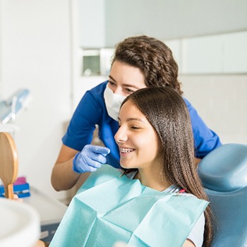 Teen and pediatric dentist smiling into small mirror