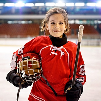 young hockey player smiling and holding their helmet