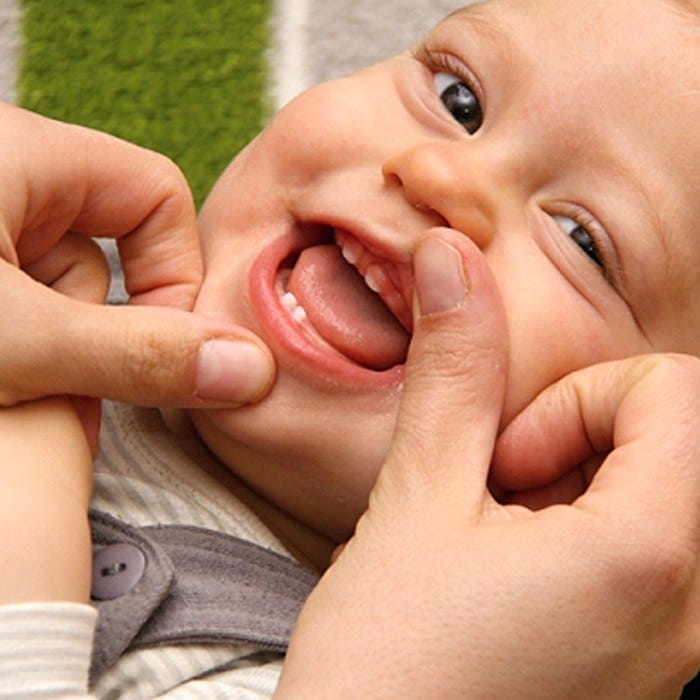 A baby laying on its back with its two top and bottom teeth exposed after seeing a dentist who offers dentistry for infants in Duncanville