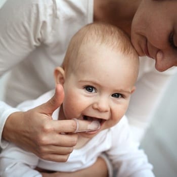 A mother using a finger brush to clean her baby’s teeth