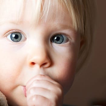 A small child holding a blanket and sucking their thumb