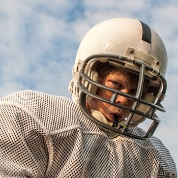 A young male teen wearing football gear and an athletic mouthguard to protect his smile