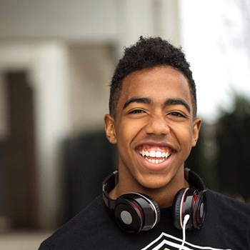 A young male teen wearing headphones around his neck and smiling after receiving fluoride treatment during an appointment with his dentist