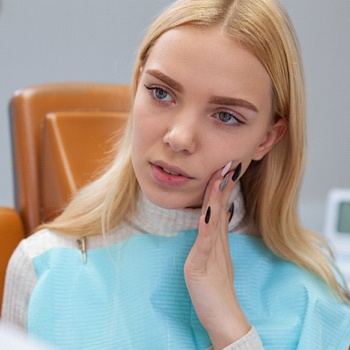 A young female holding her cheek in pain while listening to the dentist explain the necessary treatment for her dental emergency