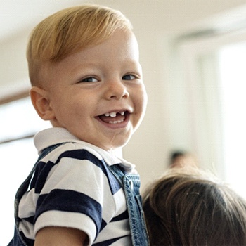 A little boy wearing denim overalls and smiling with a few missing teeth