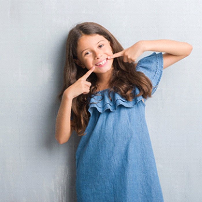 A young girl pointing to her healthy smile after seeing her pediatric dentist in Duncanville