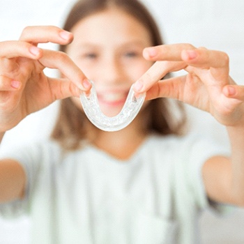 Preteen girl in white shirt holding nightguard for bruxism