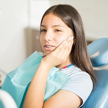 Young girl in dental chair holding cheek