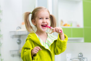 Young girl in pigtails smiling while brushing her teeth