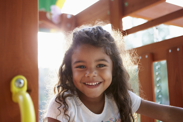 young girl with brown hair playing and smiling on a jungle gym