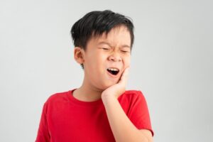 Young boy holding jaw in pain.